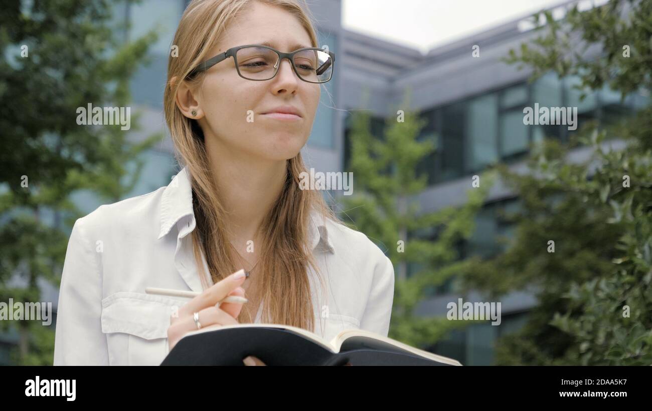 Attentive young woman having ideas and making notes in notepad Stock ...