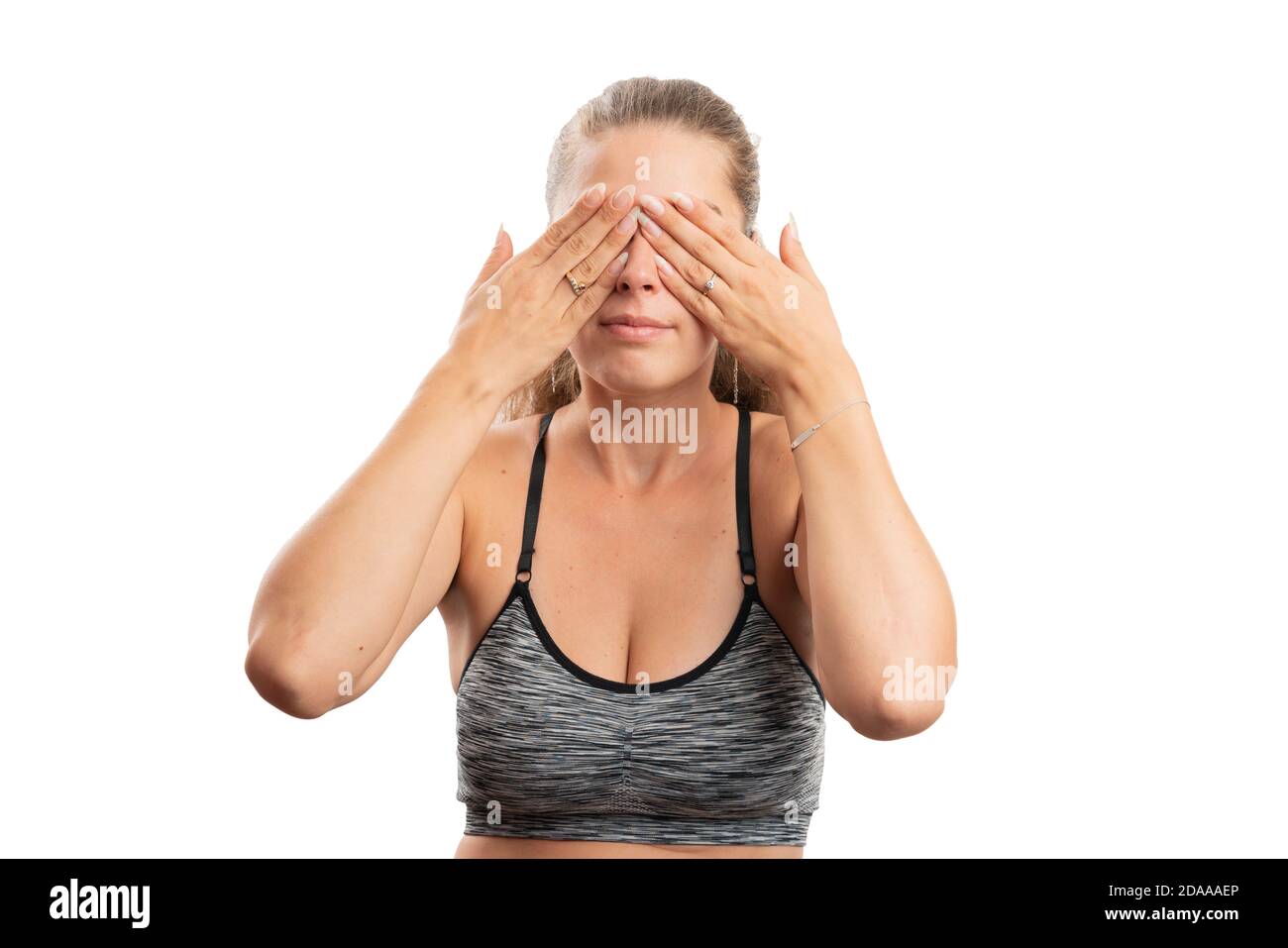 Adult model woman wearing gym training workout attire covering eyes using hands as secret concept active lifestyle isolated on white studio background Stock Photo