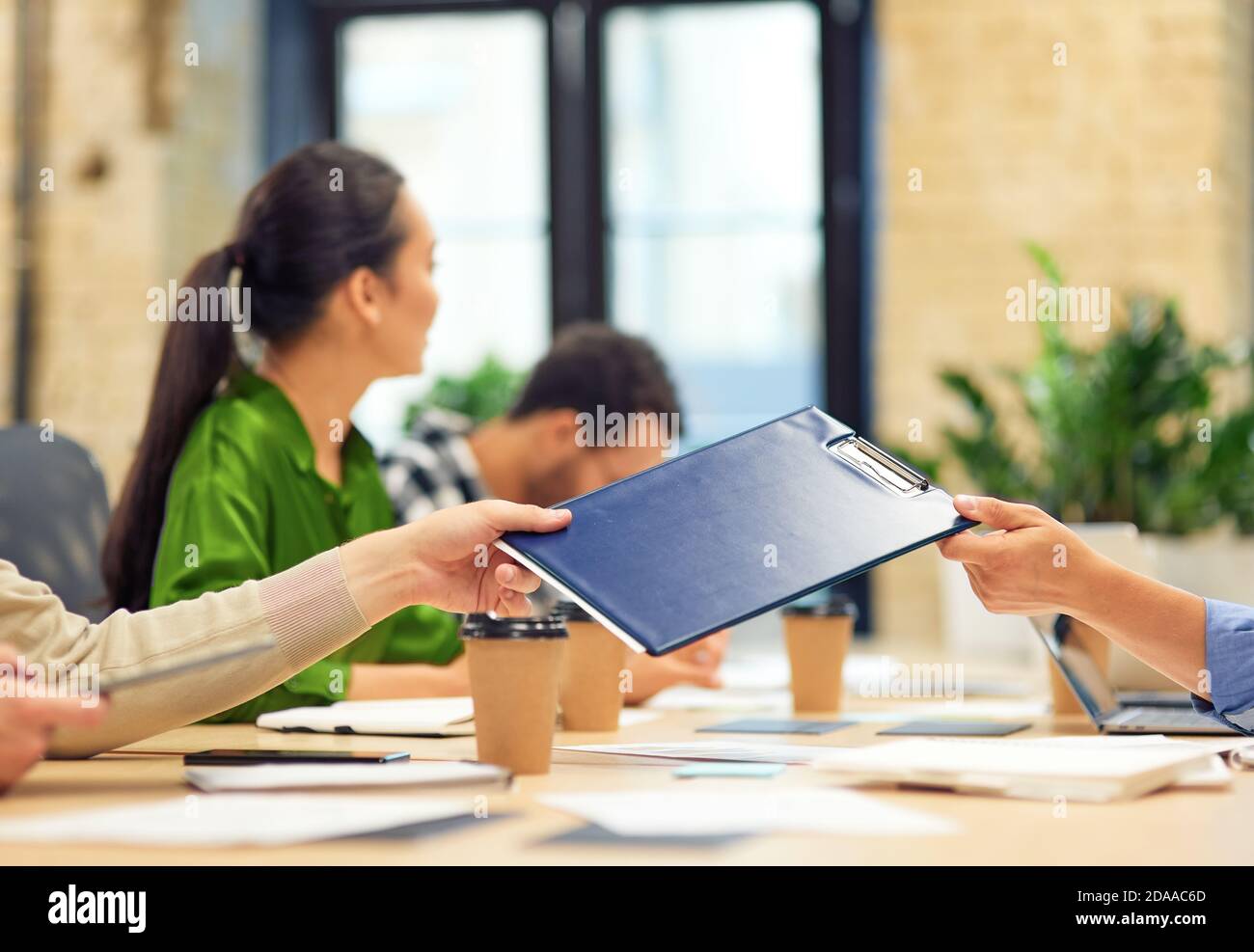 Male coworker giving a folder with documents to his colleague while working in the modern office. Teamwork and collaboration, business people concept Stock Photo