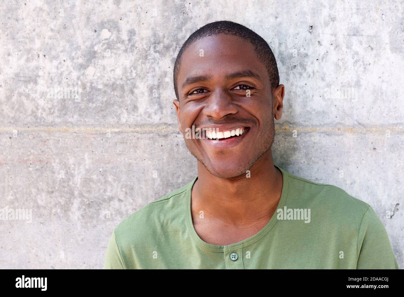 Close up portrait of cheerful young black man smiling against wall Stock Photo