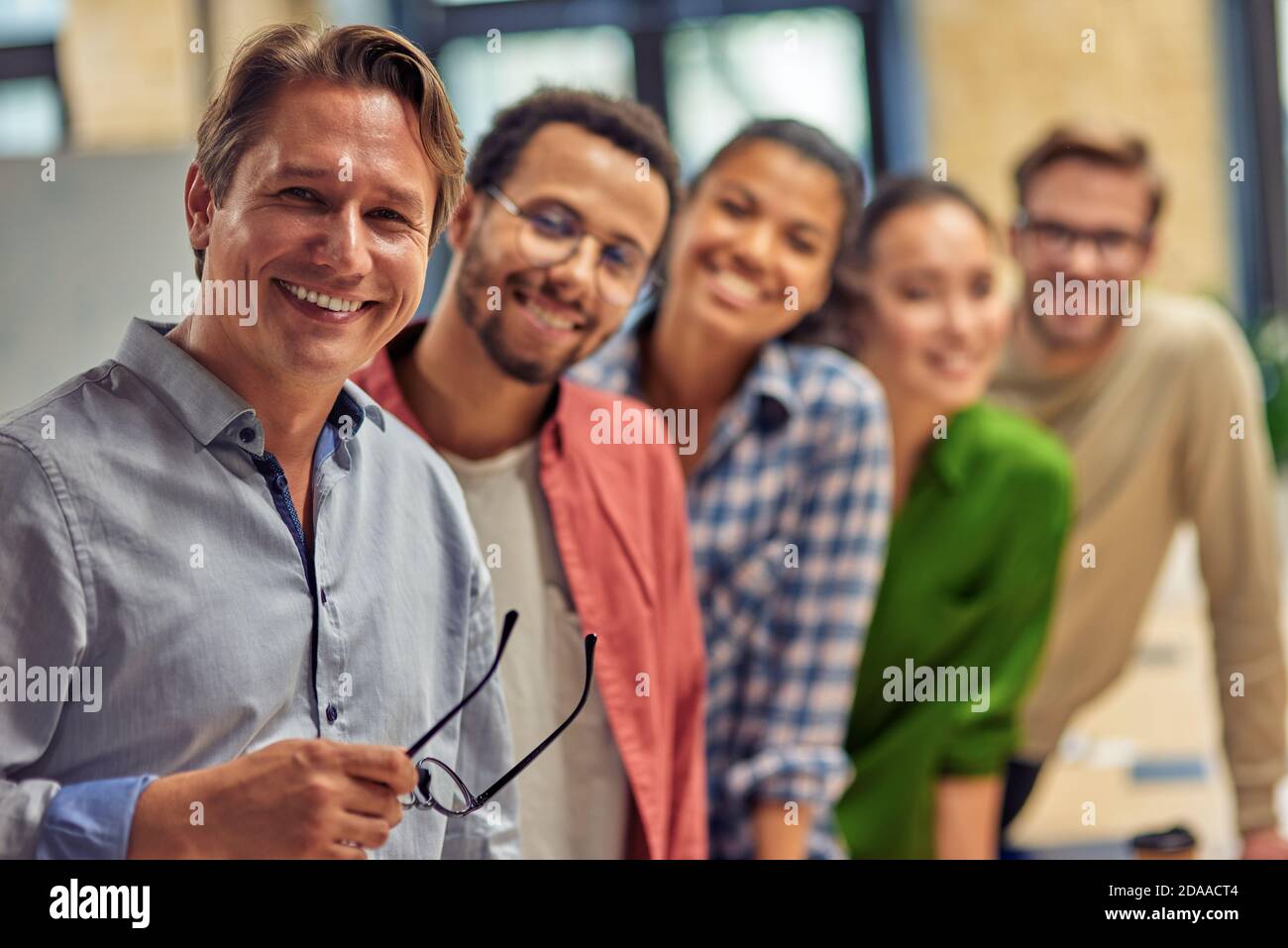 Powerful team. Group of young happy multiethnic colleagues smiling at camera while standing in the modern office, business people working together. Teamwork and cooperation concept Stock Photo