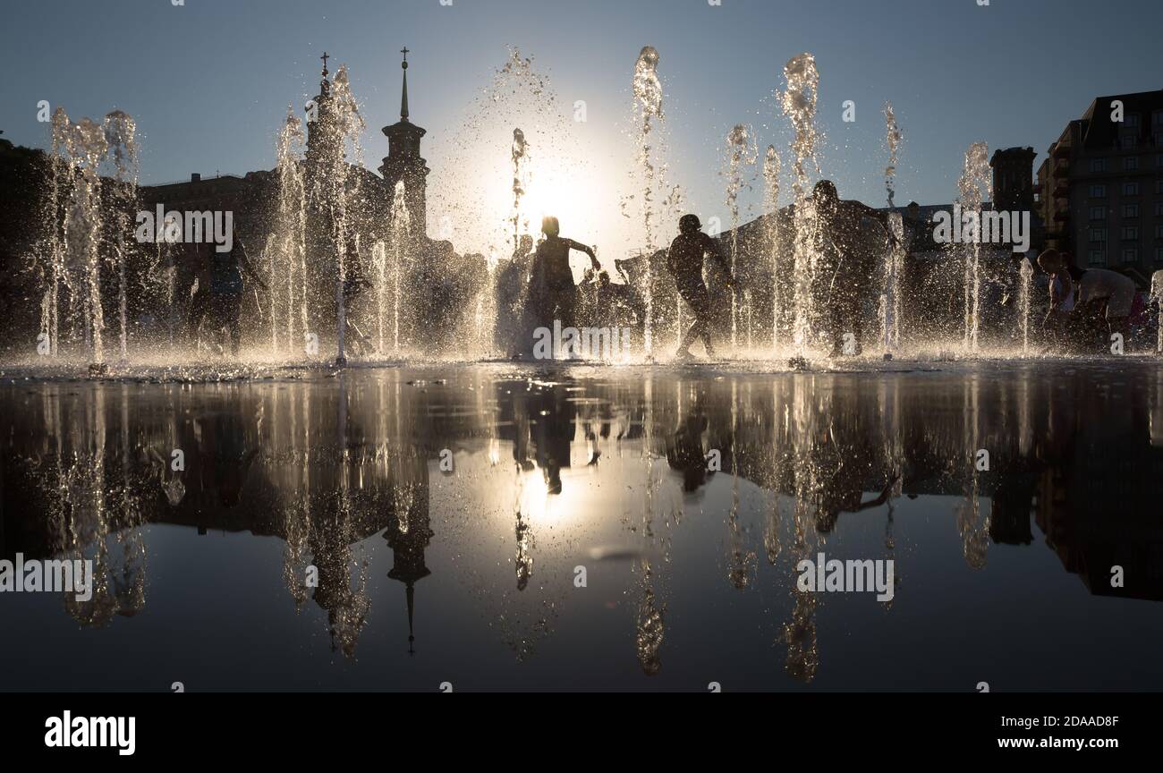 Silhouette of a group of happy children playing in a water fountain in ...