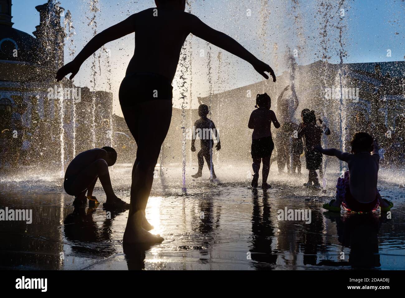Silhouette of a group of happy children playing in a water fountain in ...