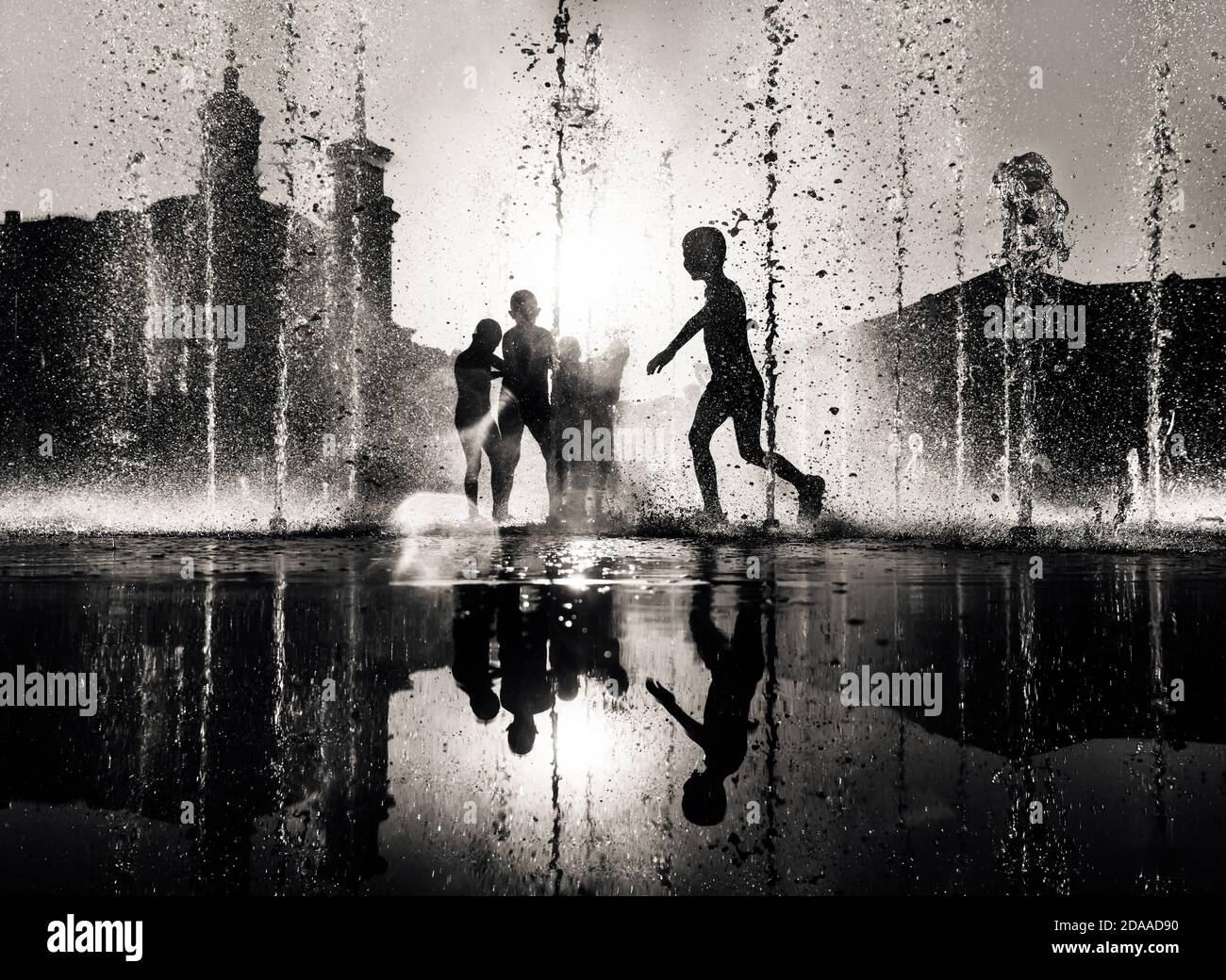 Silhouette of a group of happy children playing in a water fountain in ...