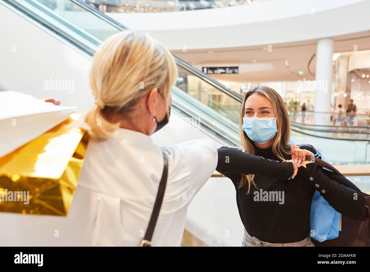 Two women with masks make elbows greeting in the shopping center at Covid-19 Stock Photo