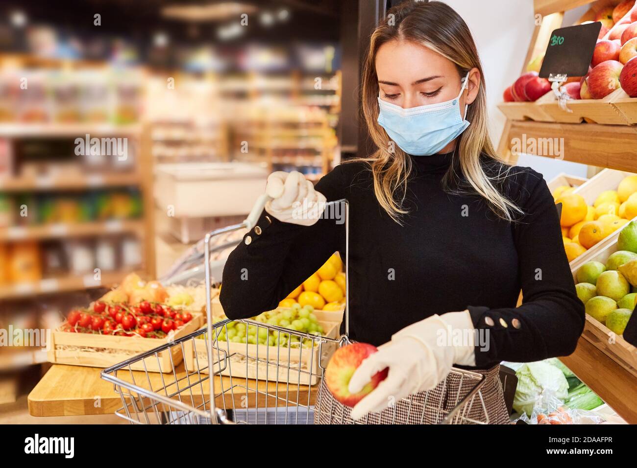 Woman as a customer with face mask when shopping in the supermarket because of the Covid-19 pandemic Stock Photo