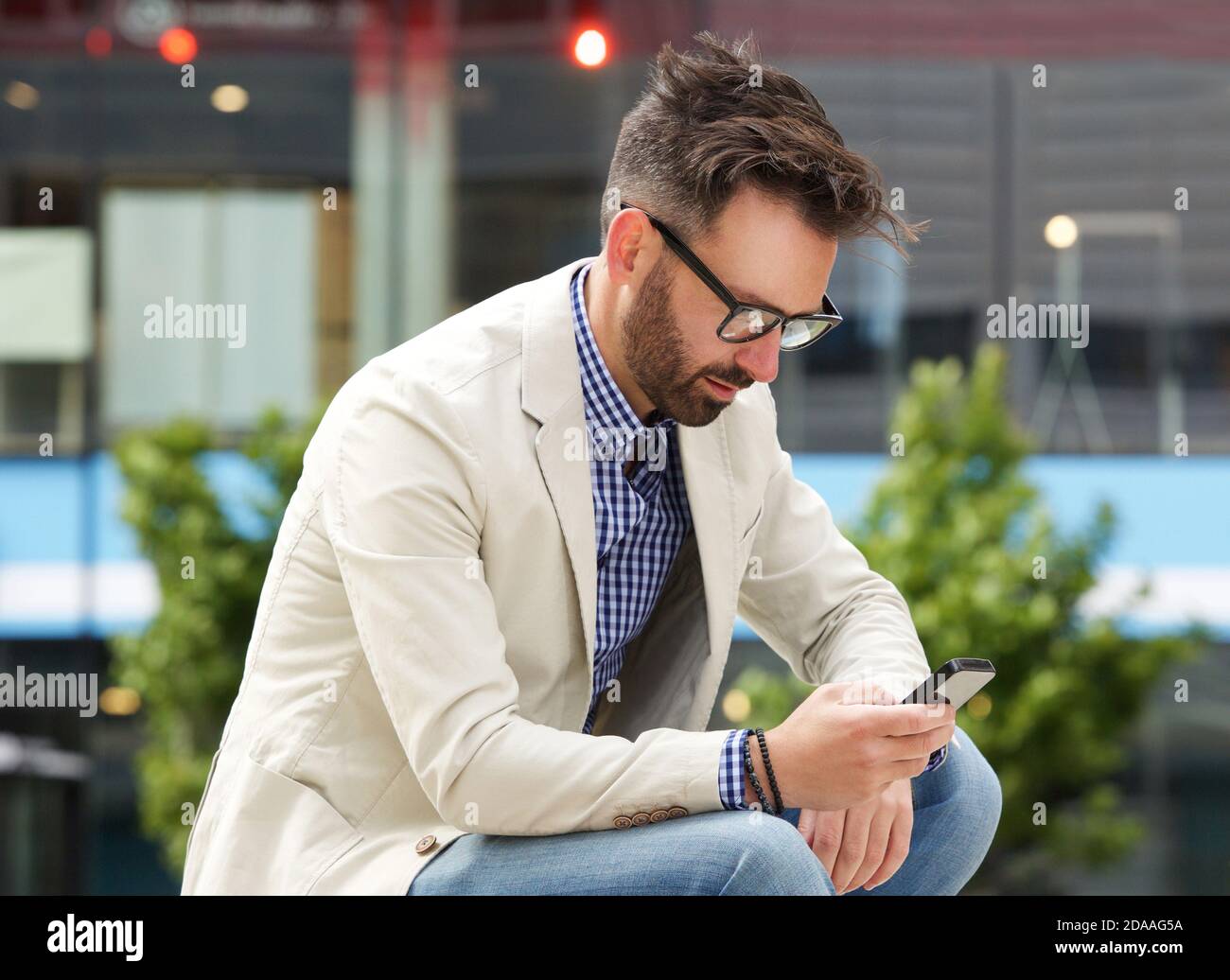 Side portrait of older man sitting outdoors and reading text message on his mobile phone Stock Photo