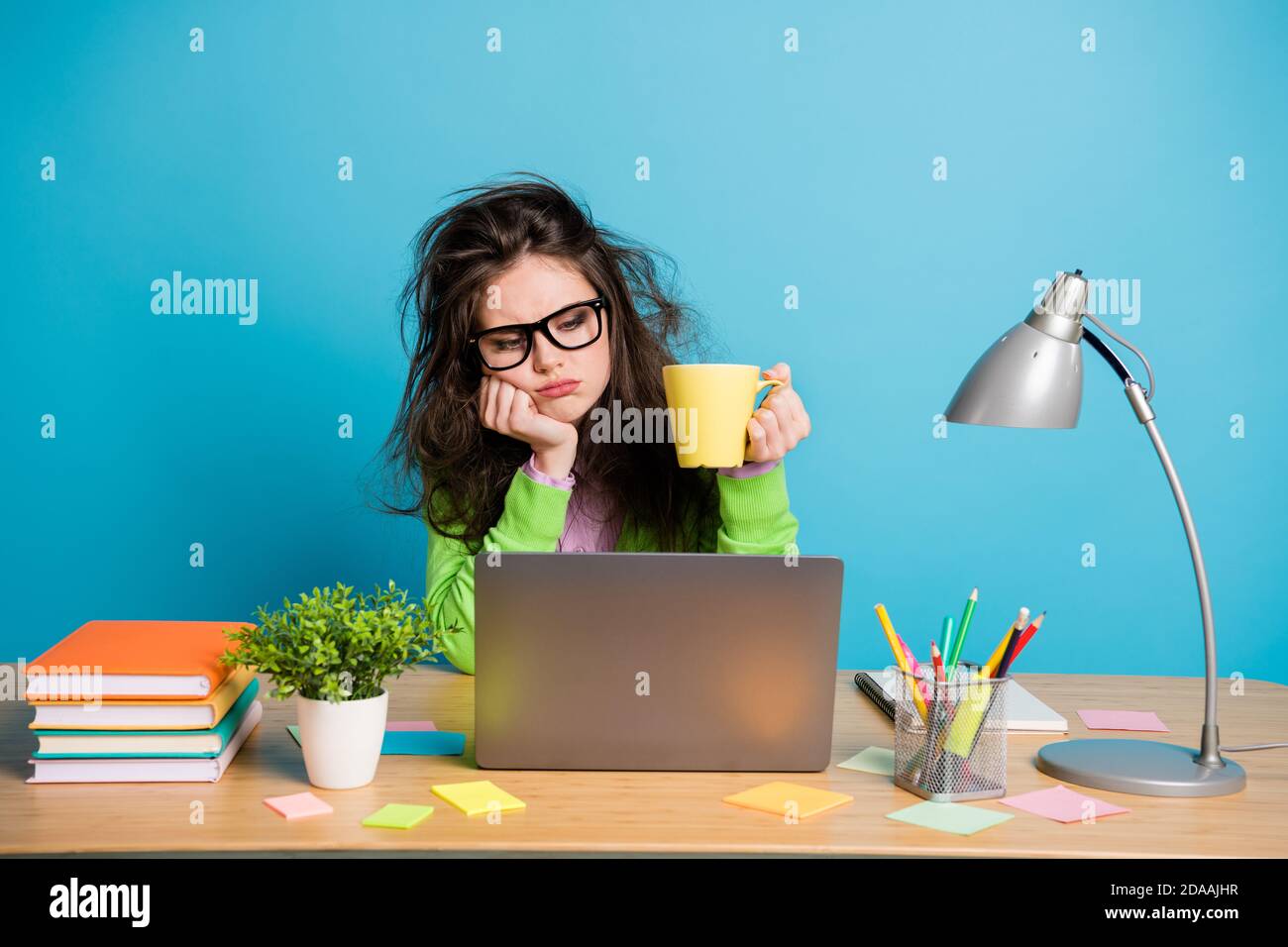 I need more coffee. Exhausted girl sit desk work remote look hold caffeine beverage mug isolated blue color background Stock Photo