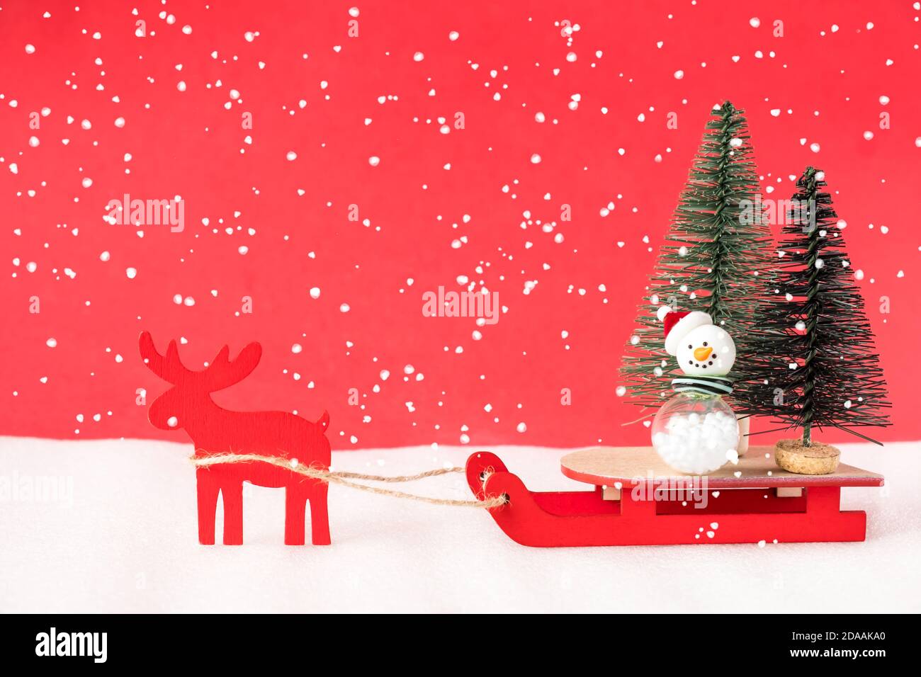Toy reindeer and sleigh delivering christmas trees on red background. Stock Photo
