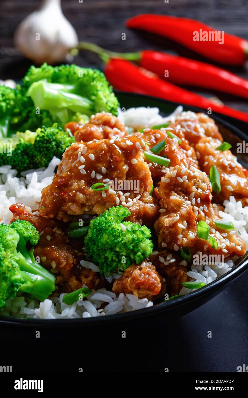 General Tso’s Chicken crispy Chinese chicken bites in a black bowl with rice and steamed broccoli florets, horizontal view from above Stock Photo