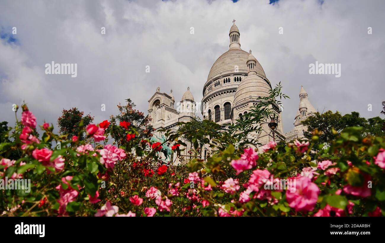 Stunning Basilica of the Sacred Heart (Sacre-Coeur Basilica) of Paris, France located on Montmartre hill, viewed from below through flower bed. Stock Photo