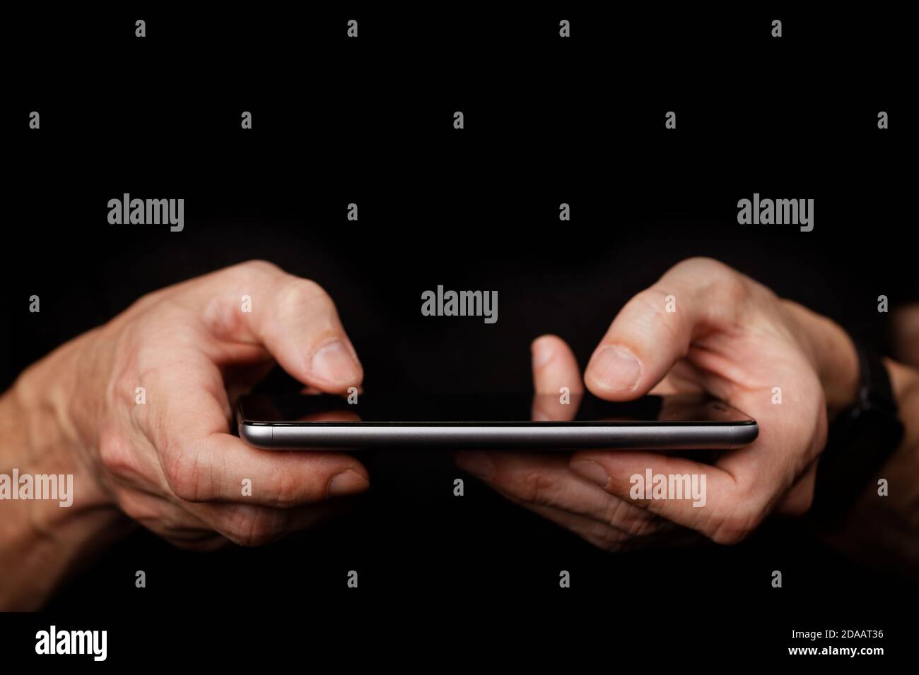 Closeup mans hand using smartphone on black background. Shallow focus. Stock Photo