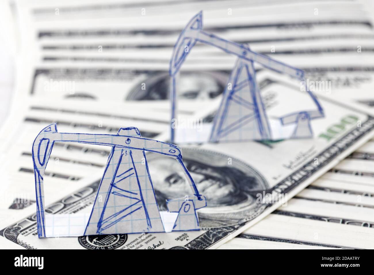 Petroleum pumpjack and oil rigs from paper on a heap of 100 dollar bills. Shallow focus. Concept image. Stock Photo