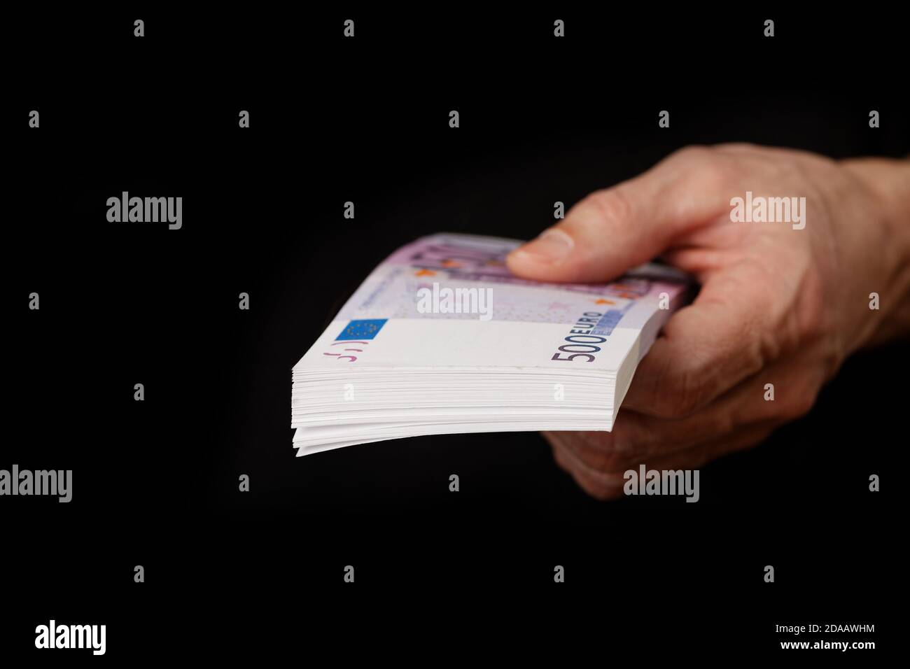 Closeup of a mans hand holding a pack of euros banknotes isolated on black background. Shallow focus. Stock Photo