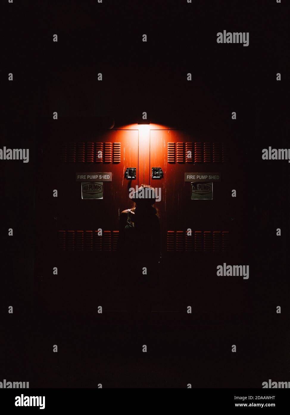 The silhouette of a girl in front of a red electrical door at night in Eastern Australia Stock Photo