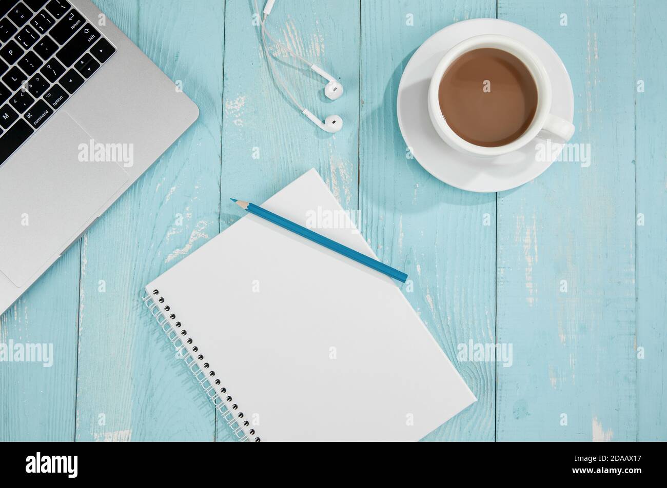 Top view of a cup of coffee, drawing notebook, laptop, and handsfree on a blue wooden surface Stock Photo