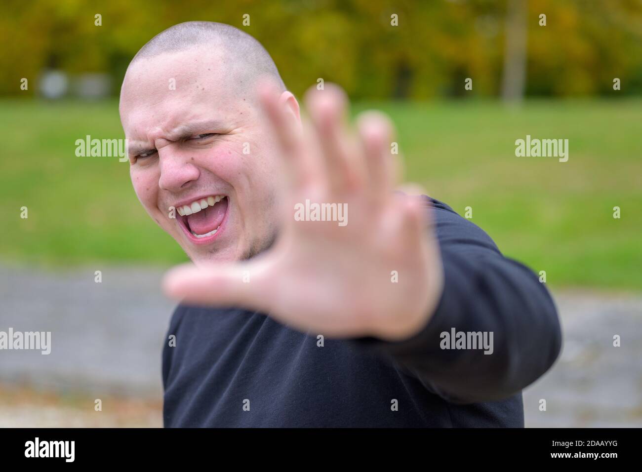 Angry young man shouting and gesturing with his hand with focus to his face outdoors in a park Stock Photo