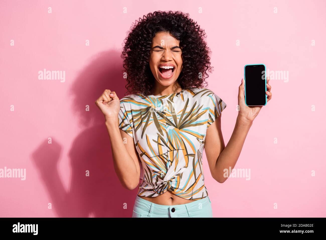 Portrait photo of shouting black skinned curly woman keeping smartphone with copyspace isolated on pastel pink color background Stock Photo