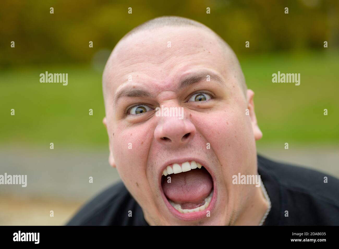 Young man with shaved head asserting his dominance yelling threateningly at the camera in frustration outdoors in a park Stock Photo
