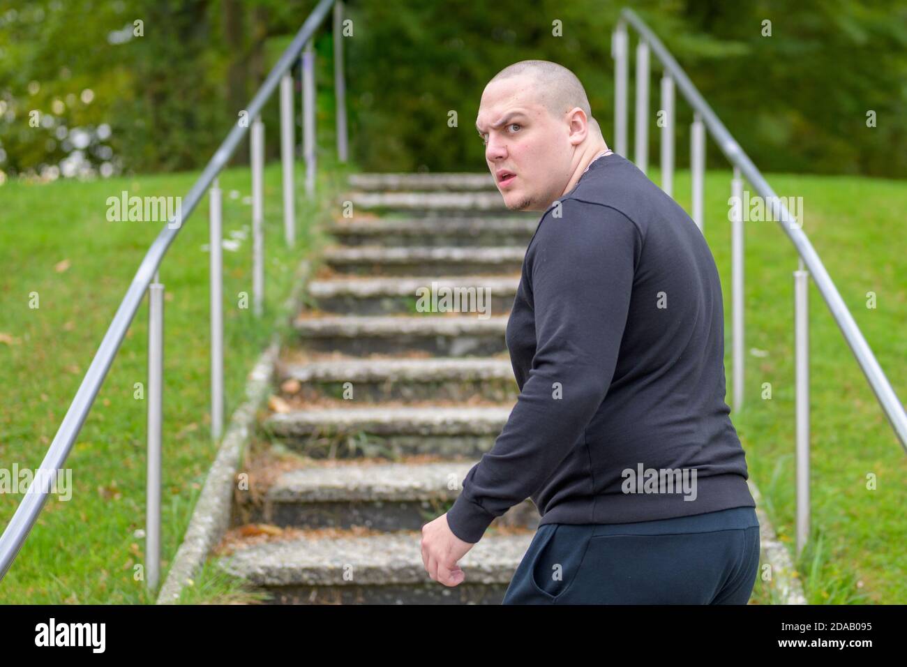 Angry aggressive young man turning to yell at the camera with a look of fury as he walks up steps in a green park Stock Photo