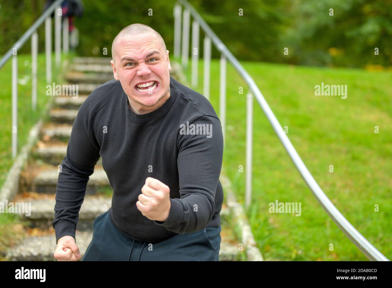 Angry man threatening the camera with his fist as he screams abuse with a vehement expression on outdoors steps in a park Stock Photo