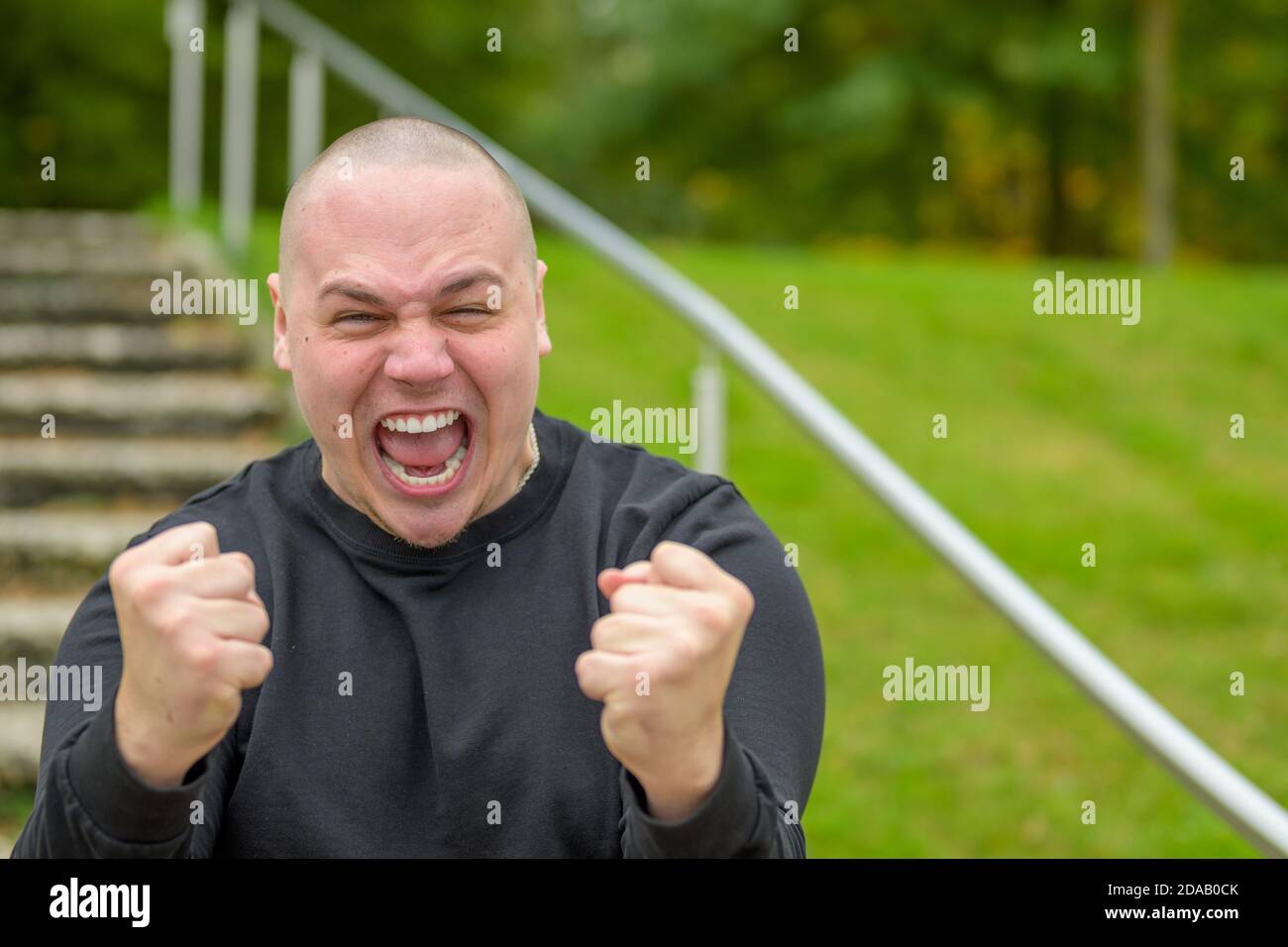 Frustrated angry man yelling at the camera in a rage and clenching his fists in a menacing gesture outdoors in a park Stock Photo