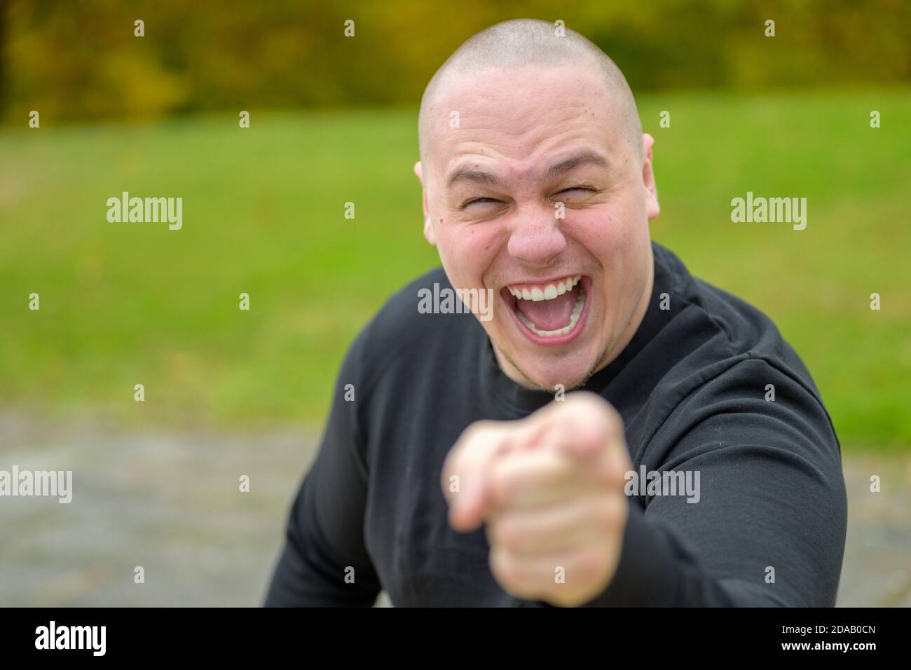 Emotional young man laughing or shouting at the camera while pointing his finger with focus to his face outdoors in a park Stock Photo