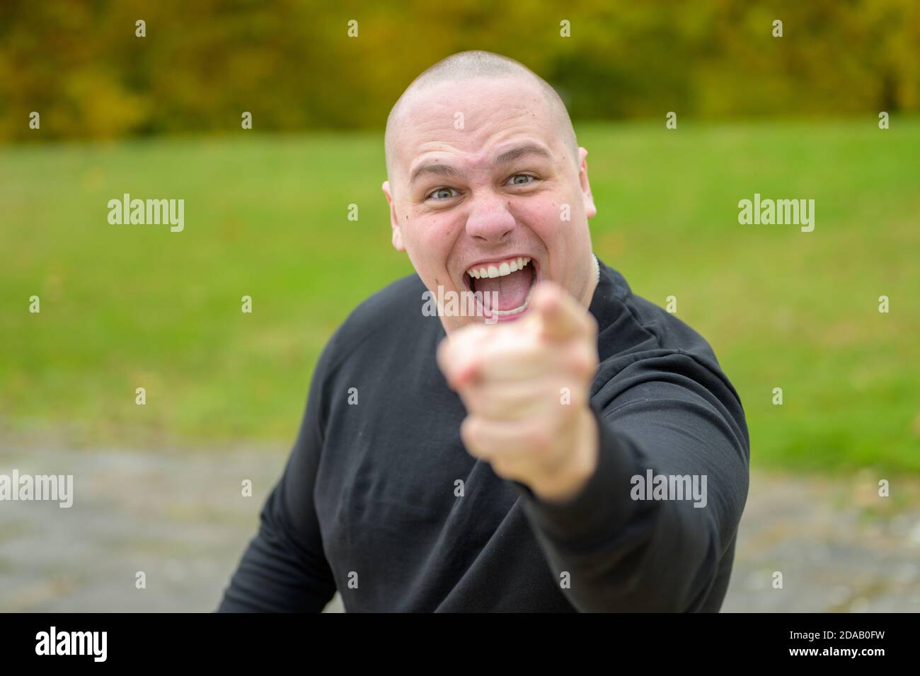 Emotional young man laughing or shouting at the camera while pointing his finger with focus to his face outdoors in a park Stock Photo