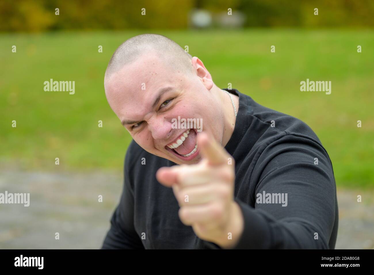 Angry man with shaved head pointing a finger of blame at the camera while voicing his aggression outdoors in a park Stock Photo