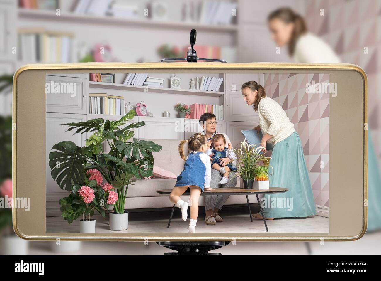 Young female blogger online influencer mom with grandmother and two daughters, live streaming a parent playing with children show on social media usin Stock Photo