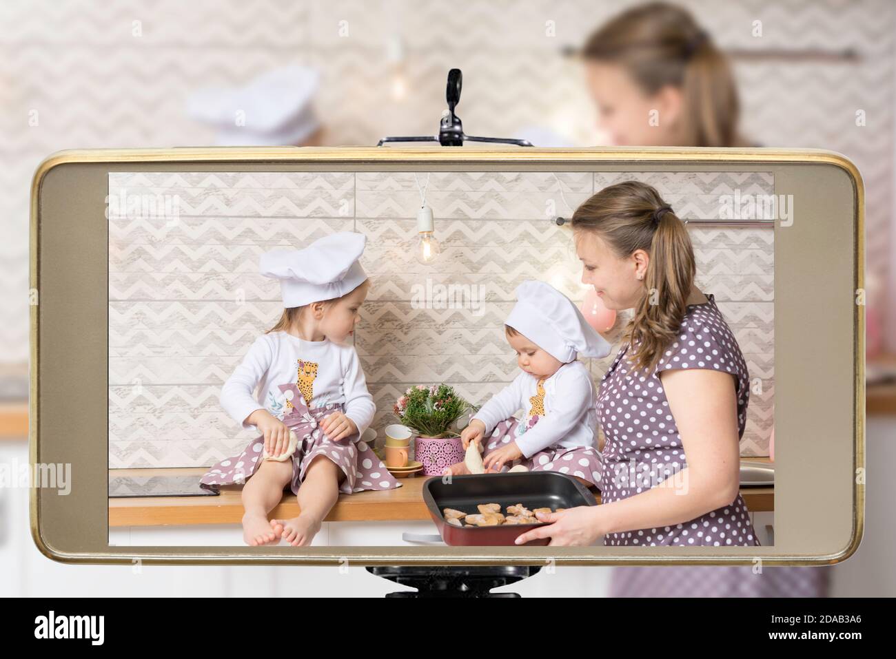 Young female blogger and vlogger online influencer mom with two daughters, live streaming a cooking, baking cookies with children show on social media Stock Photo