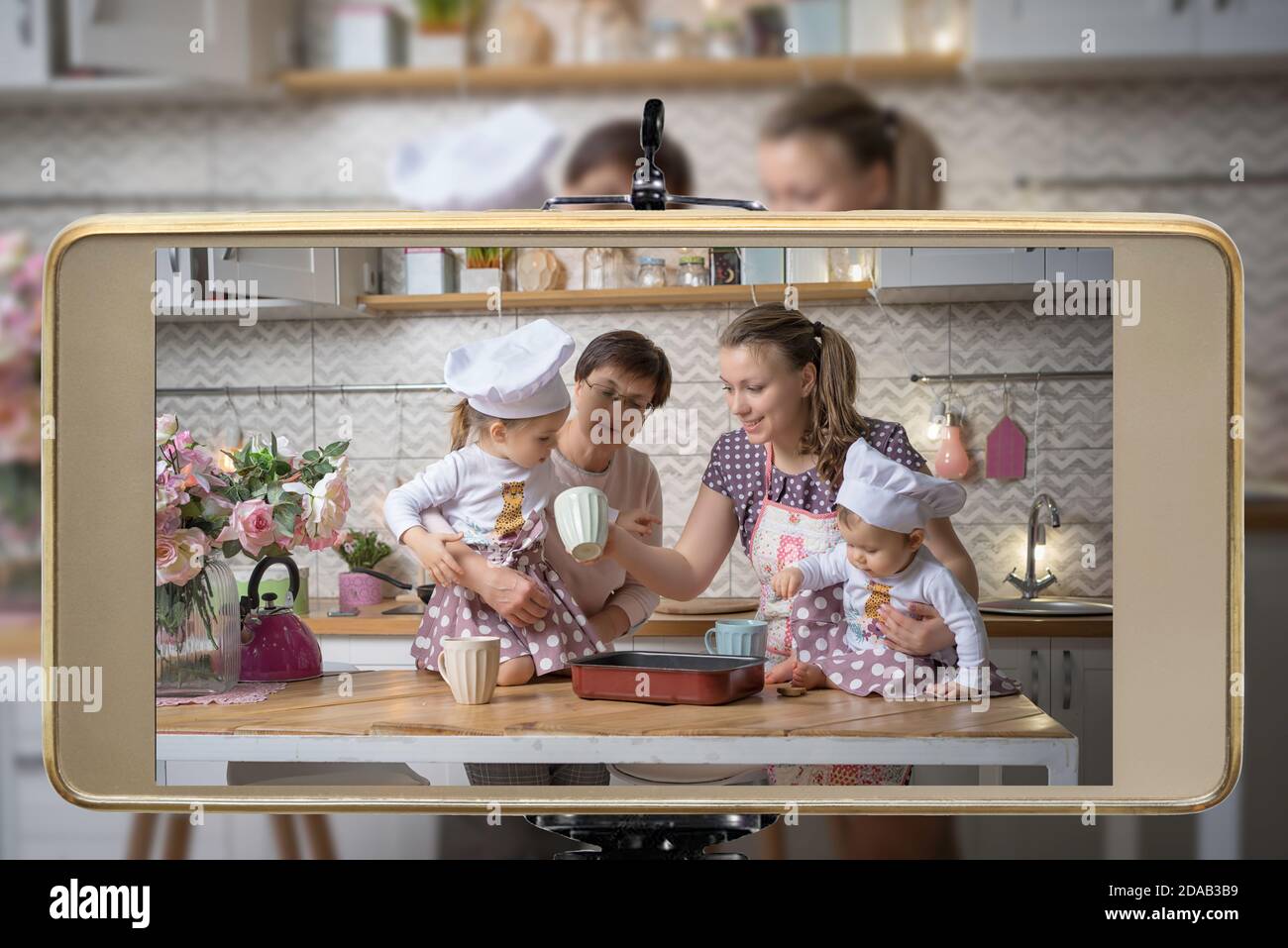 Young female blogger and vlogger online influencer mom with grandmother and two daughters, live streaming a cooking with children show on social media Stock Photo