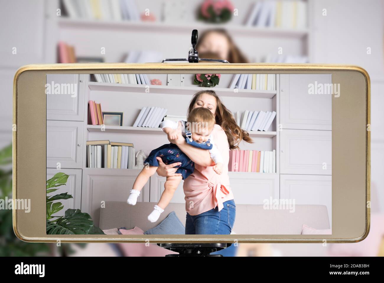 Young female blogger and online influencer live streaming parenting show on social media using a smartphone. Stock Photo