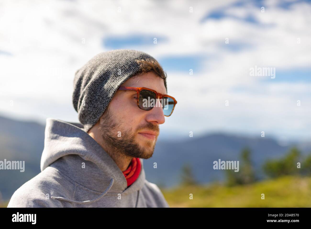 Attractive young white man wears sunglasses with a hat and a hoodie on a nice sunny day in nature Stock Photo