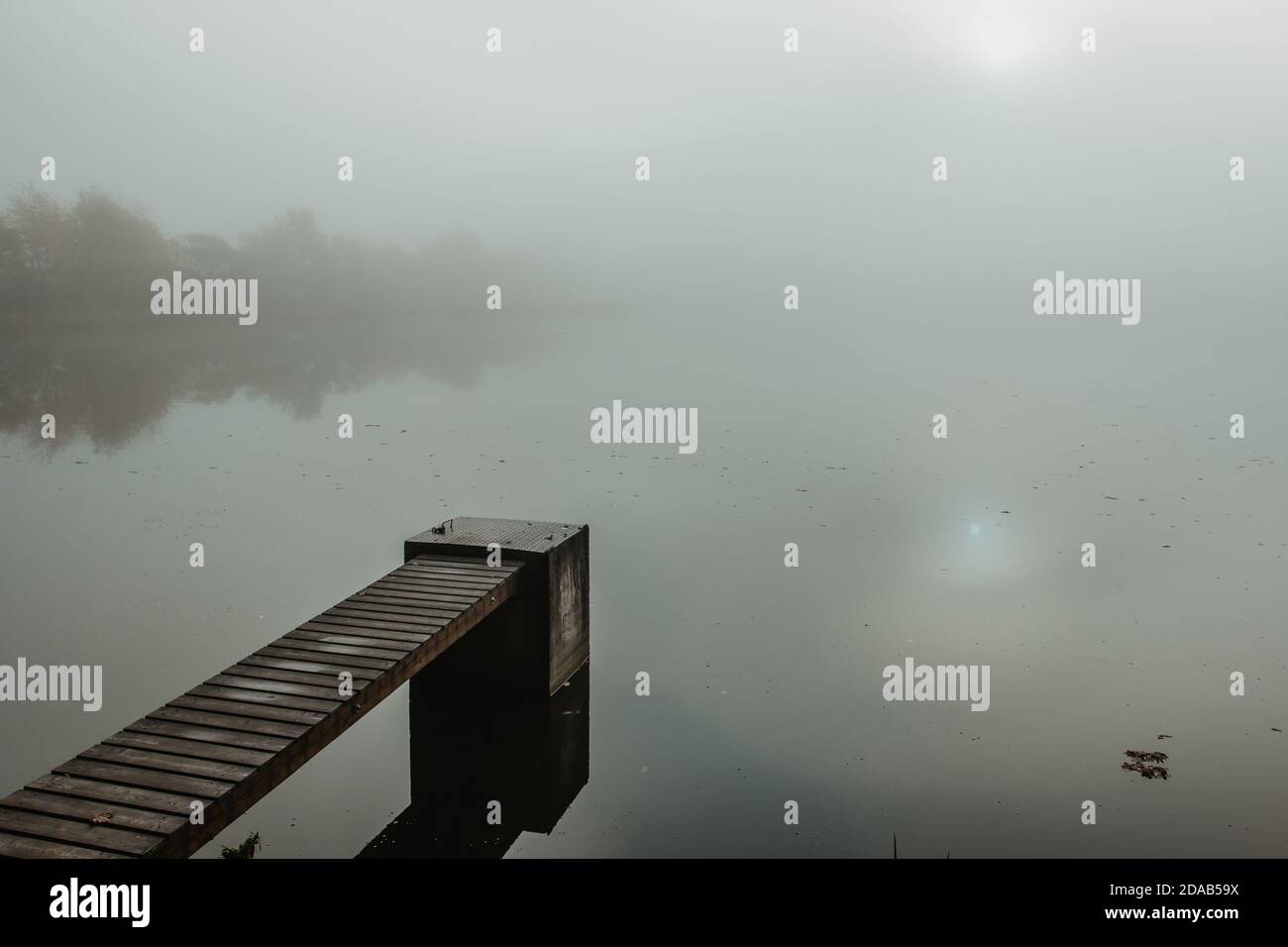 Mysterious morning by lake. Foggy autumn mystery atmosphere. Wooden pier on the pond.Magic mood. Misty fall day. Speechless place. Relaxing meditation Stock Photo