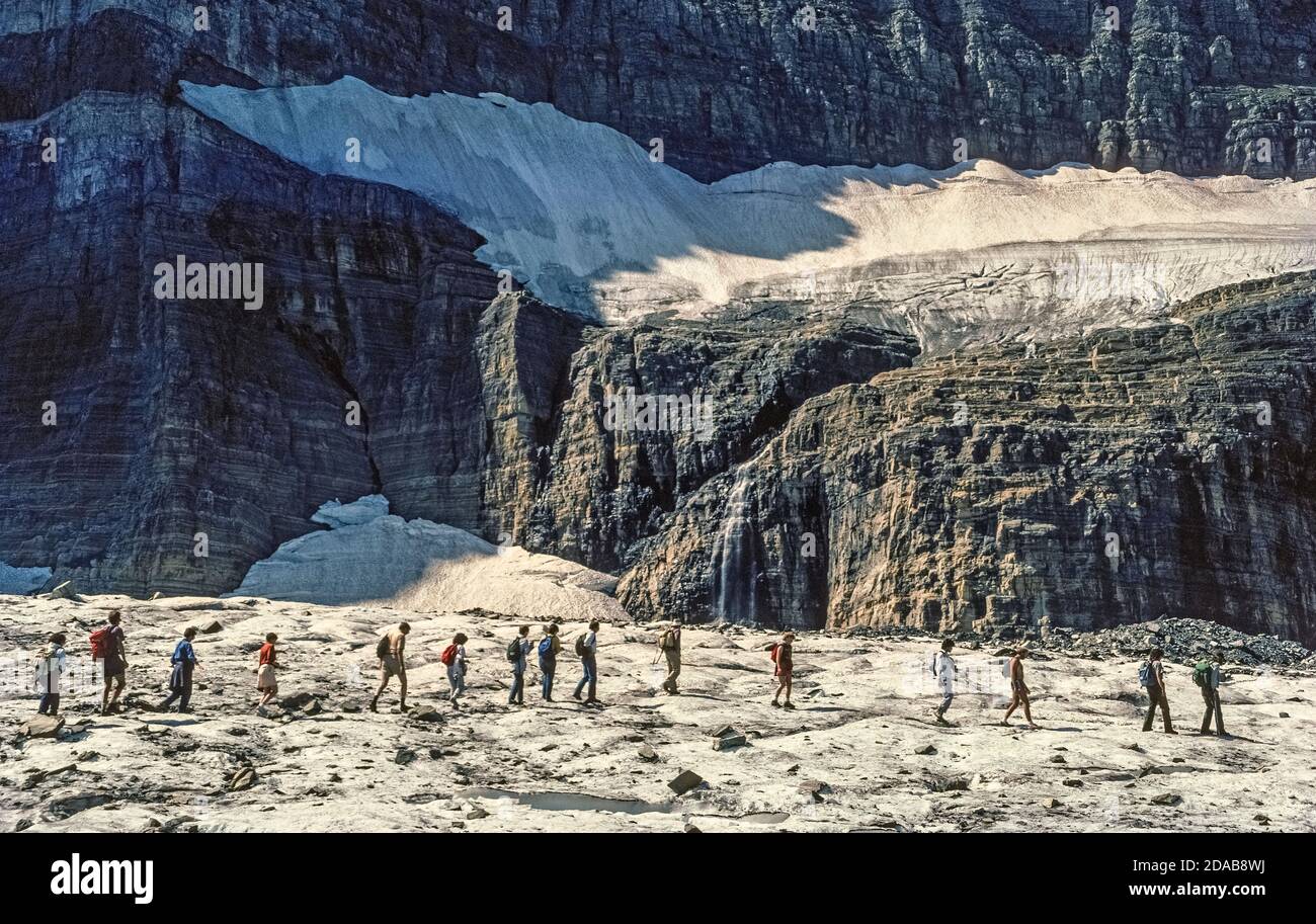 A line of hikers on a ranger-led tour cross an icy remnant of the receding Grinnell Glacier, a longtime attraction in Glacier National Park, a vast wilderness preserve in northwestern Montana, USA. The glacier was named for George Bird Grinnell, an early conservationist who discovered the ice field in 1885 and helped the pristine region to be established as America's 10th national park in 1910. Unfortunately the numerous glaciers for which the park is named have suffered from climate change over the years. From an estimated 146 glaciers in the mid-19th century, only 26 named glaciers remain. Stock Photo