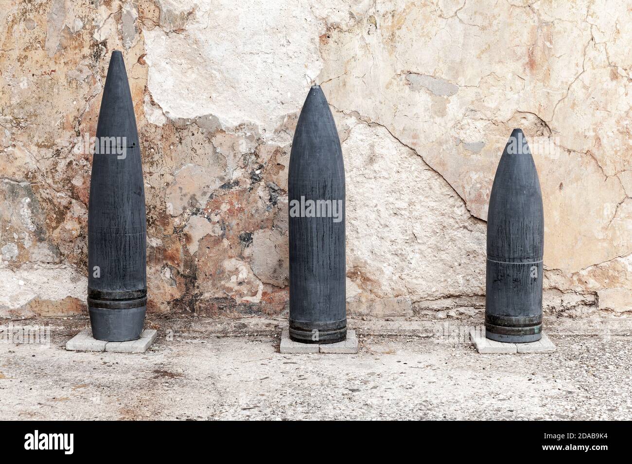 Dark large caliber artillery projectiles stand near grungy wall in a row Stock Photo