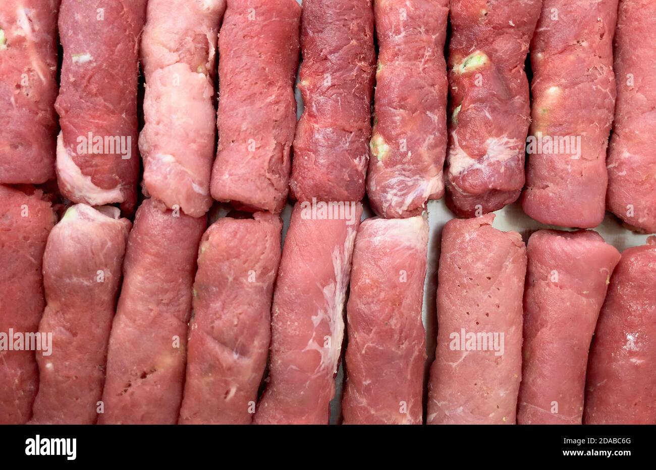Blanks of round meat sausages are stacked in a row. Cooking meat dishes