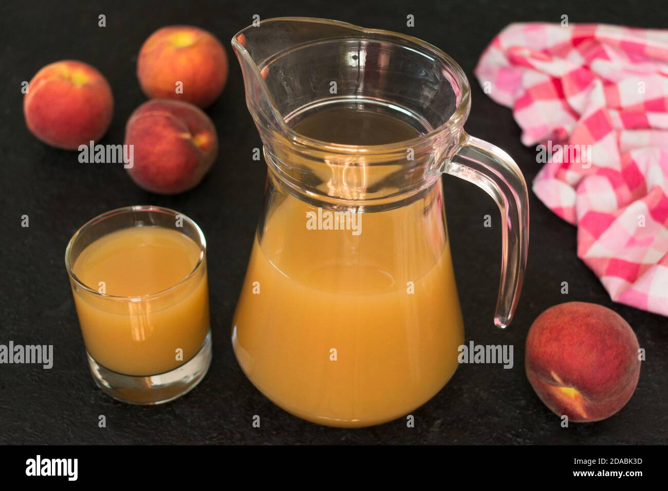 Peach juice in a jug and ripe peaches on a black background. Stock Photo