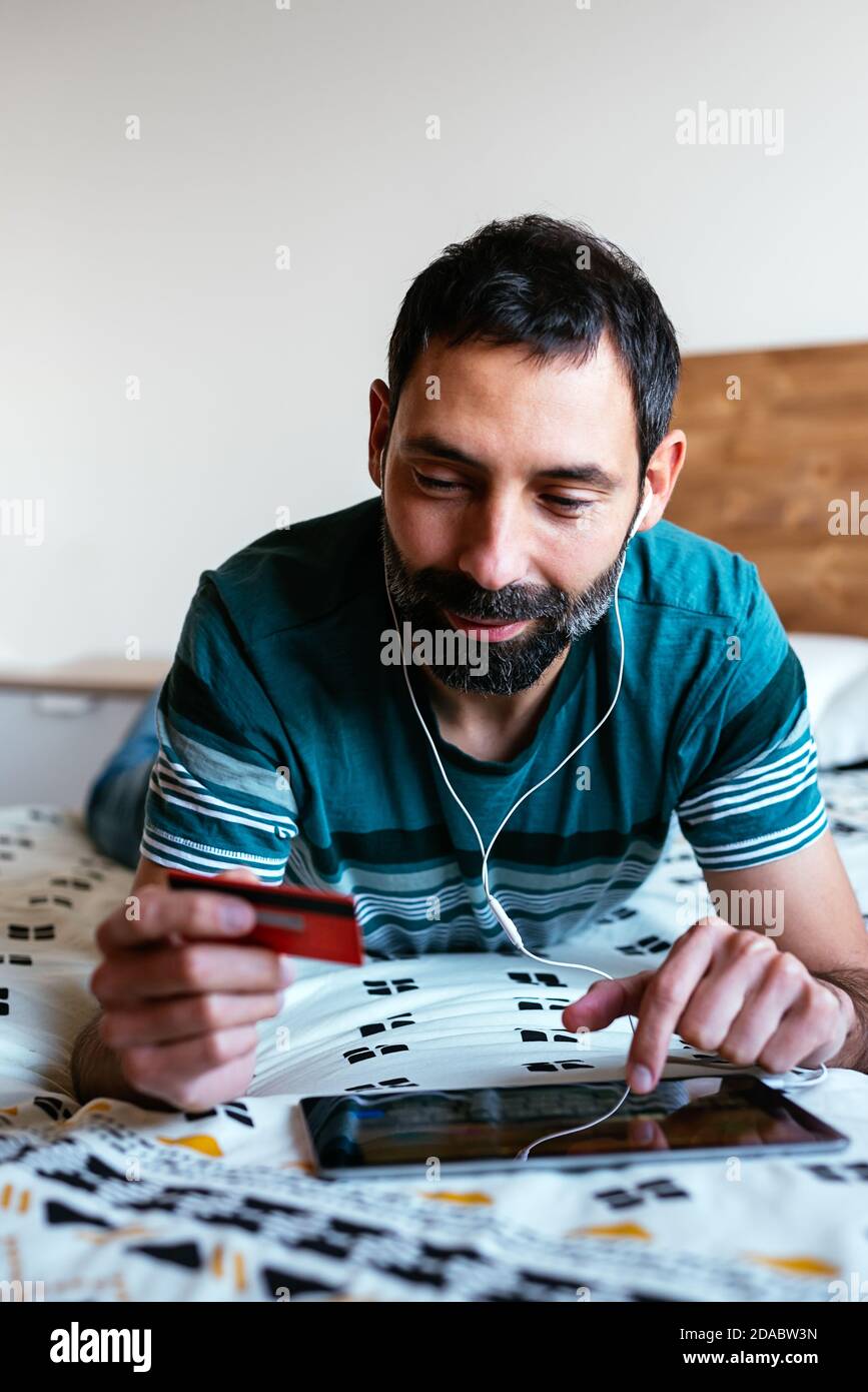 Man shopping online on a tablet lying on the bed at home Stock Photo