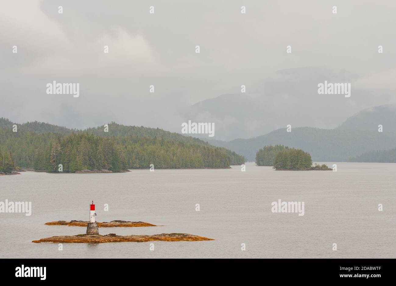 Scenic view from the ferry to the Inside Passage off Vancouver Island. In foreground a rock with a beacon. In background wooded islands and mountains. Stock Photo