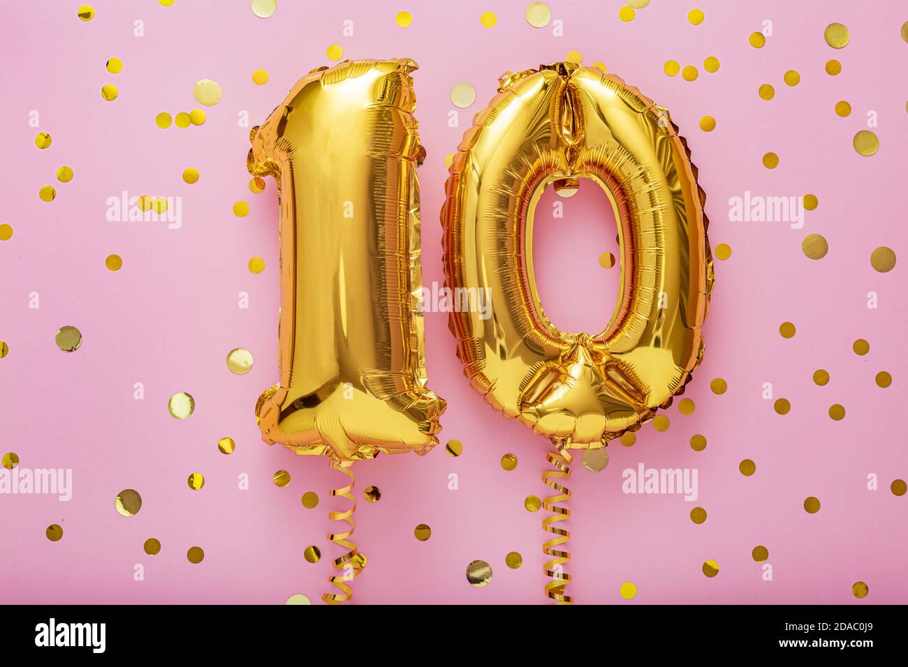 10 air balloon numbers on pink background. 10 k gold foil balloons with confetti. Birthday party flat lay with copy space Stock Photo