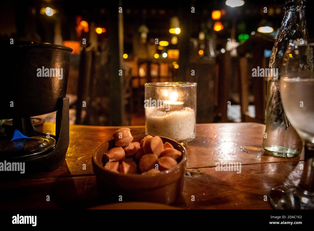 Tealight inside a glass illuminating a dark scene among different objects and food for a fondue Stock Photo