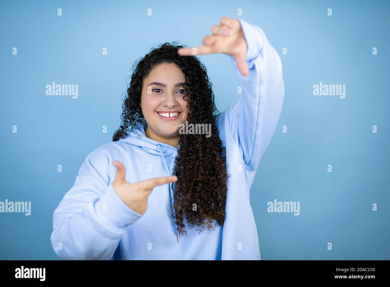 Young beautiful woman wearing casual sweatshirt over isolated blue background smiling making frame with hands and fingers with happy face Stock Photo