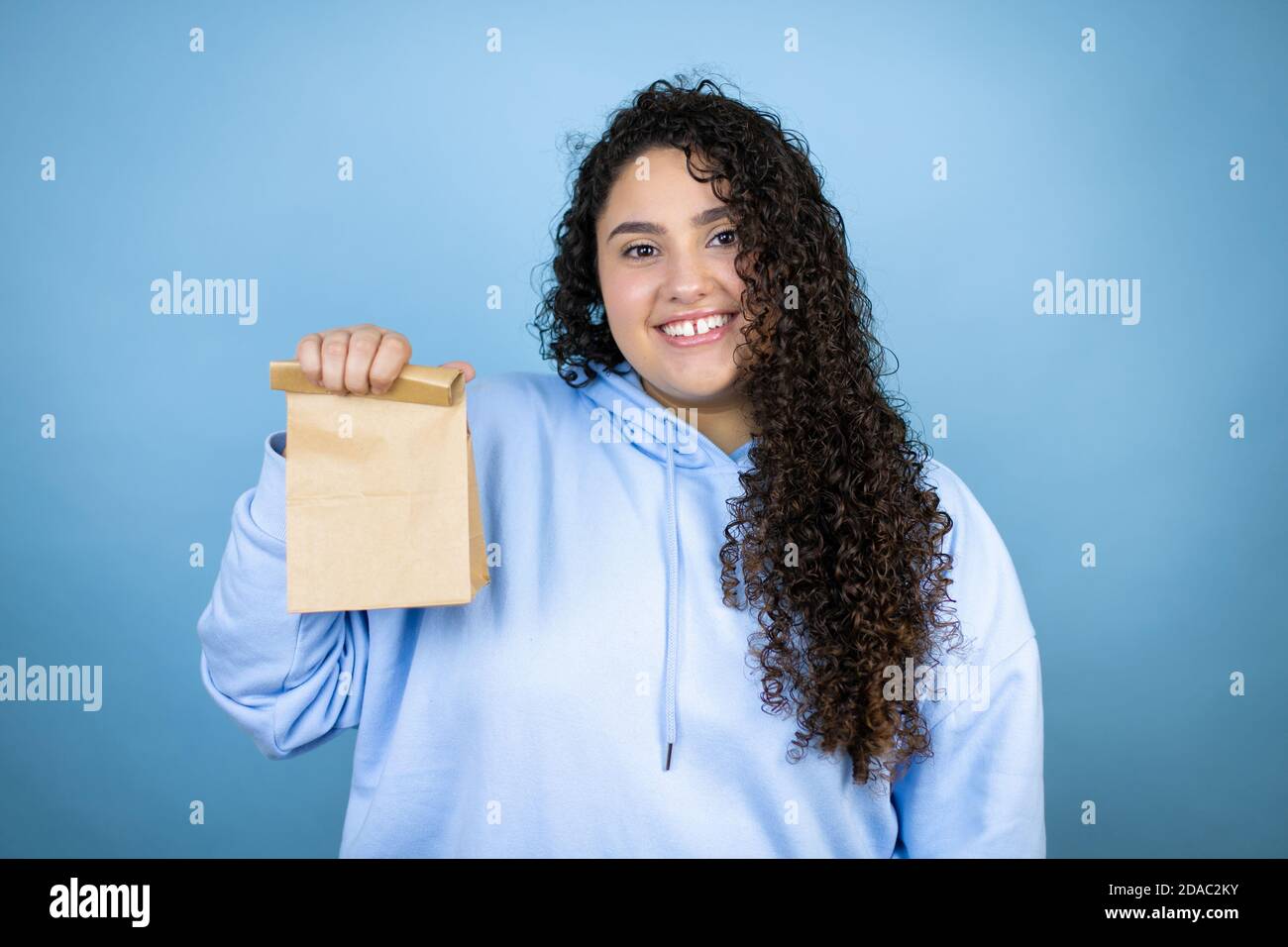 https://c8.alamy.com/comp/2DAC2KY/young-beautiful-woman-wearing-casual-sweatshirt-over-isolated-blue-background-smiling-and-holding-a-paper-bag-2DAC2KY.jpg