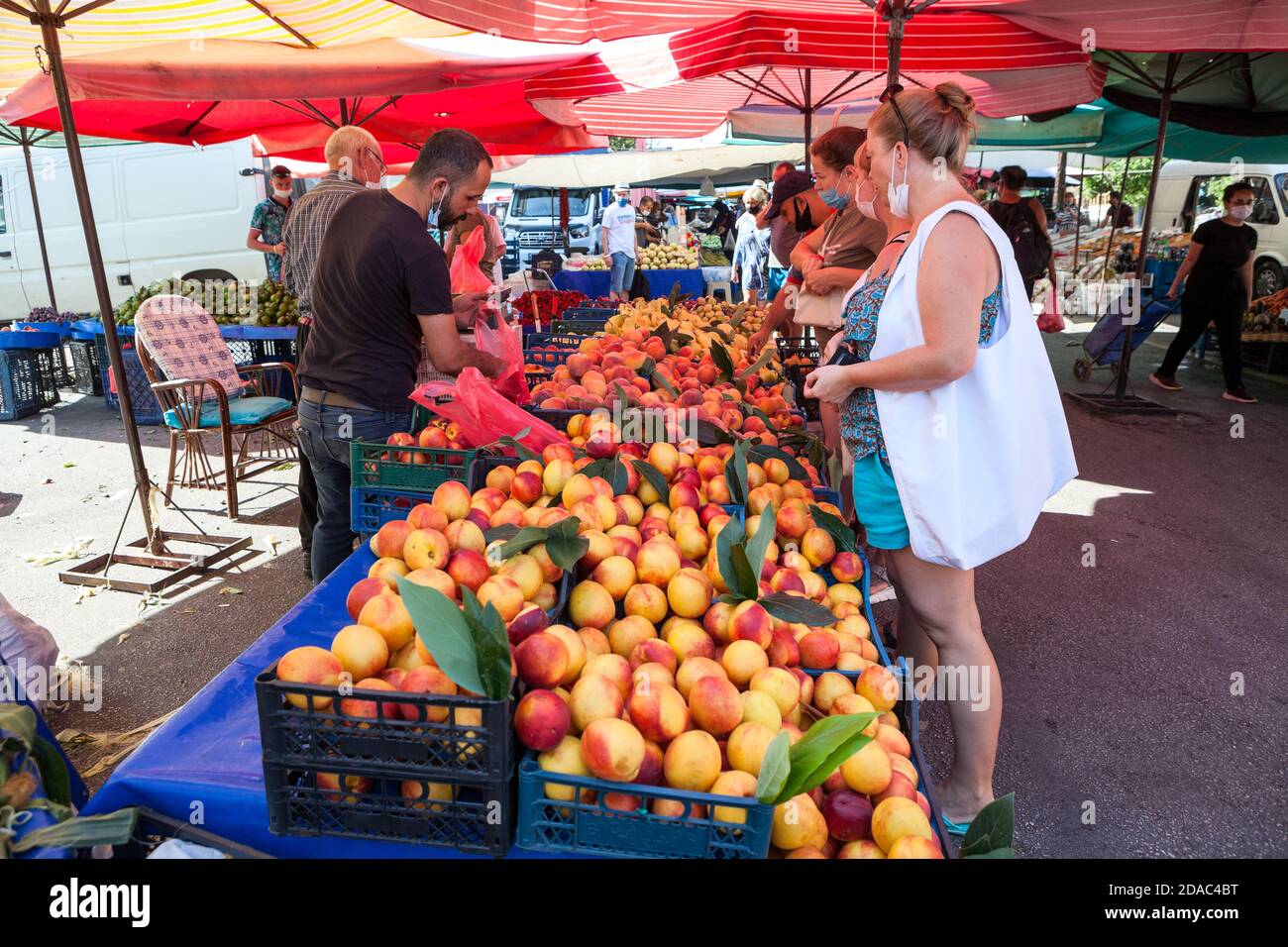 Caucasian adult women buy peaches in local market in city. Seasonal vegetables and fruits are on sale in large bazaar. Alanya, Turkey Stock Photo
