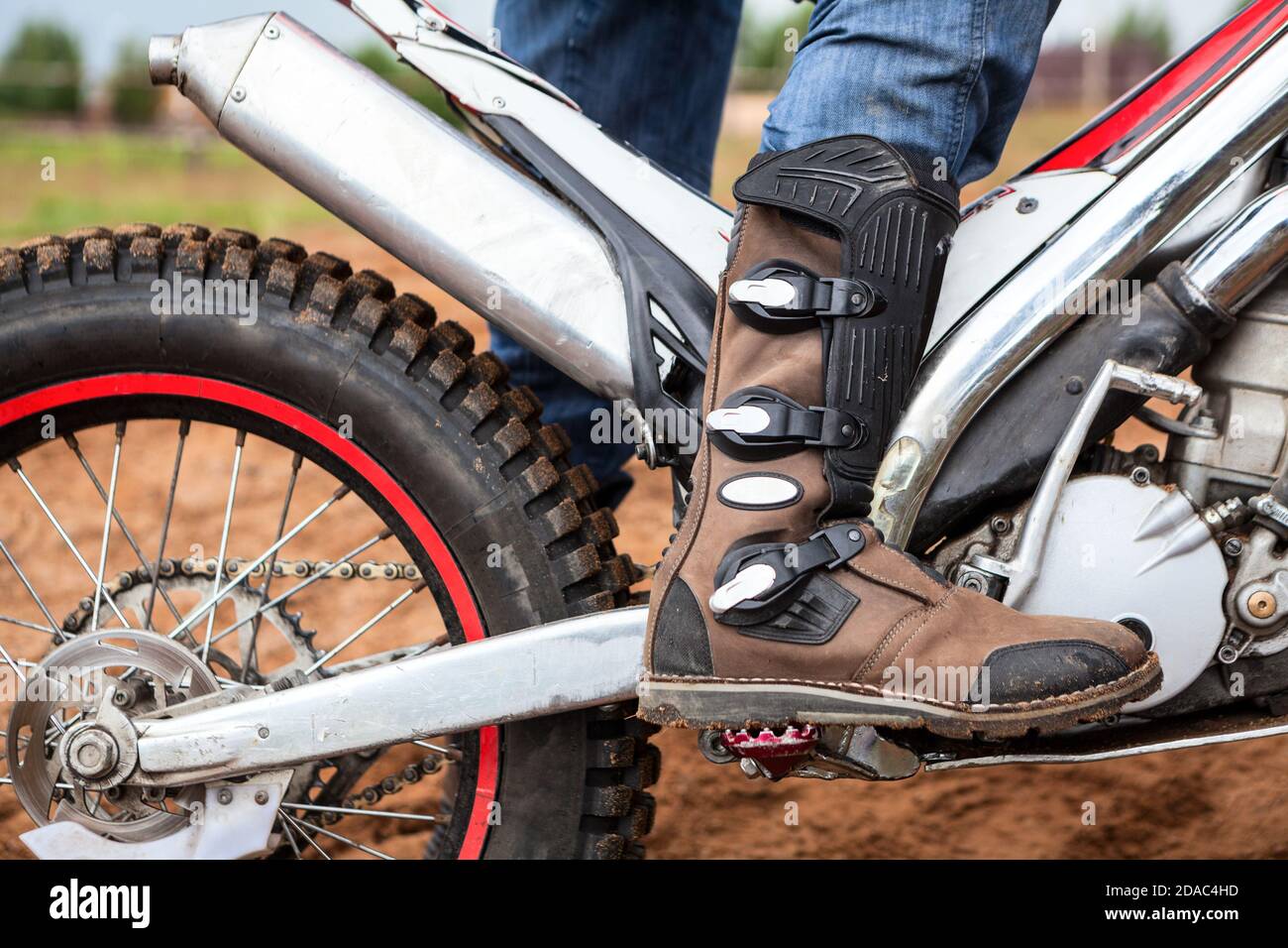 Closeup view at rider's motocross boot standing on peg of dirt motorcycle. Safety apparel for
