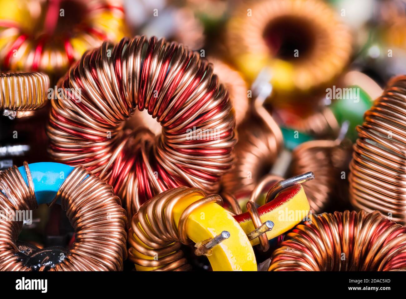 Toroidal electronic inductors on heap. Electrotechnical background. Closeup of beautiful induction coils. Copper wire winding on magnetic ferrite core. Stock Photo