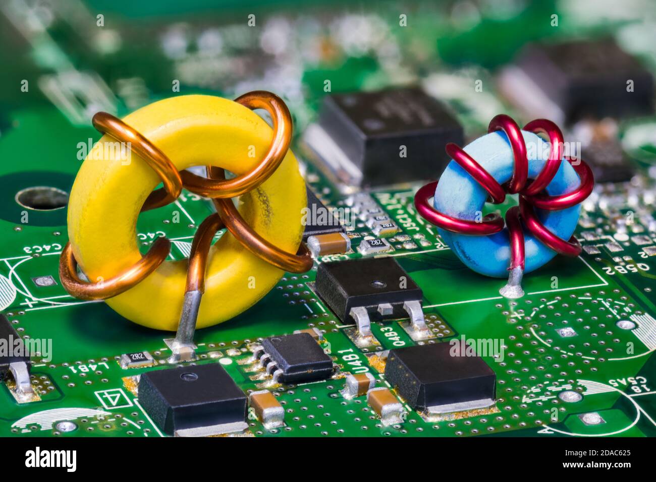 Two toroid inductors and electronic transistors on a green circuit board. Beautiful yellow or blue induction coil on PCB in embedded voltage converter. Stock Photo