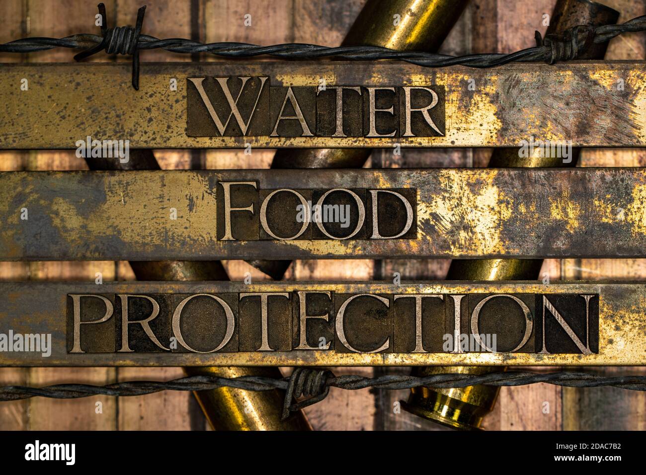 Water Food Protection text message over 50 caliber rifle cartridges on vintage textured grunge copper background lined with barbed wire Stock Photo
